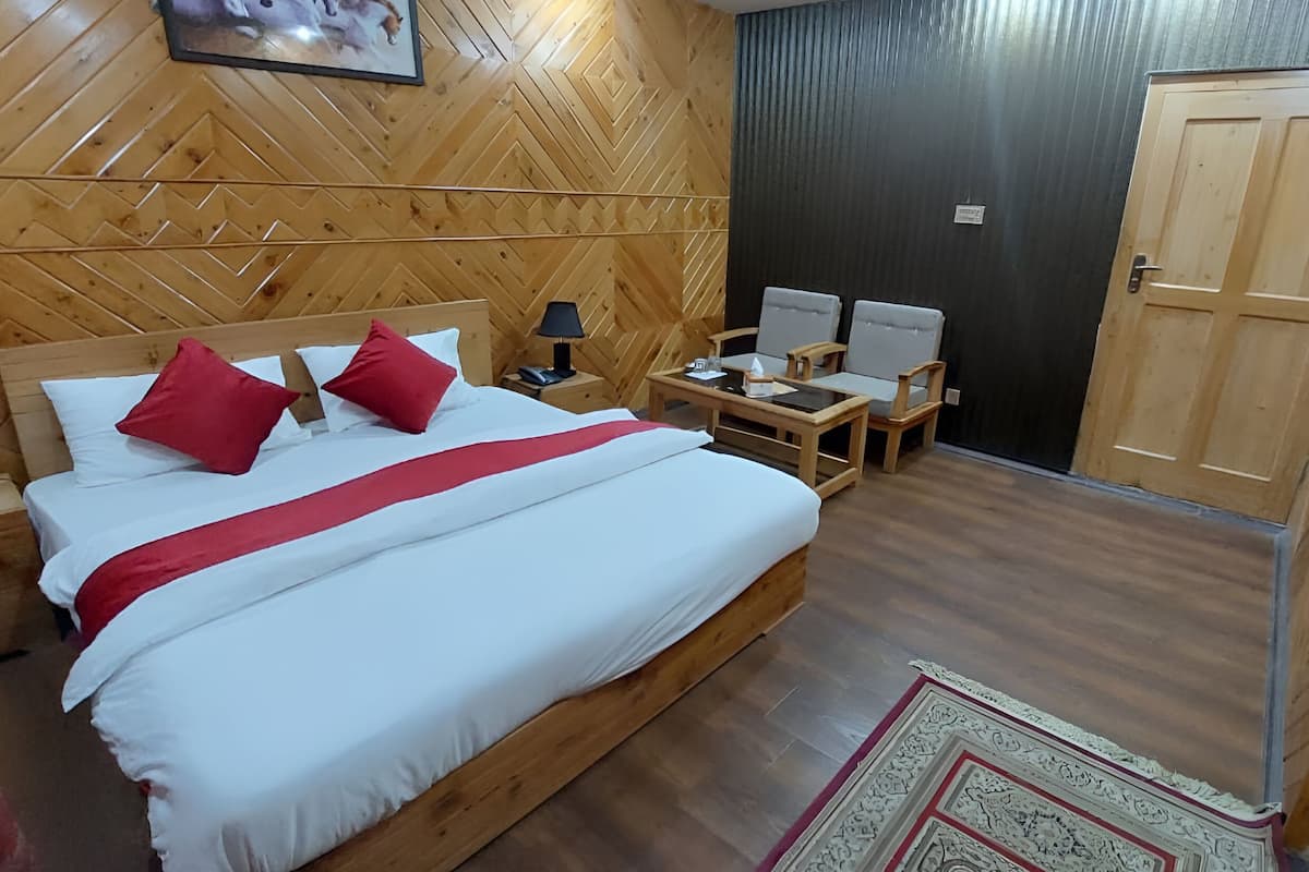 Een kamer met houten lambrisering, een bed, twee stoelen, een tafeltje en een deur.