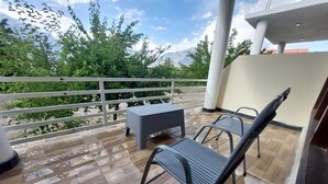 A balcony with wooden flooring, metal chairs, a small table, and a white railing.