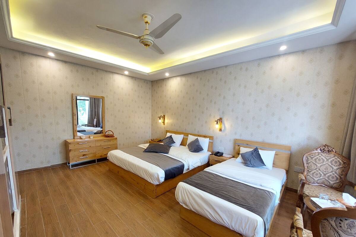 Een hotelkamer met twee bedden, houten vloeren, een plafondventilator en een grote spiegel.