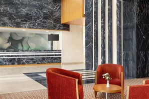 A lobby with marble walls, a reception desk, and red upholstered chairs.
