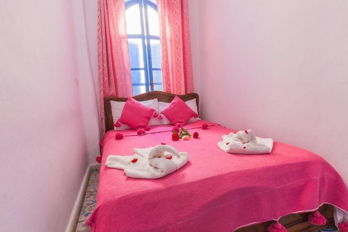 A bed with a pink bedspread, two white towels, and pink pillows.