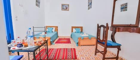 Een knus kamertje met twee bedden, een bureau en een stoel. Er hangt een spiegel aan de muur en op een tafeltje staan een waterfles en andere spullen.