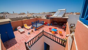 A rooftop terrace with a blue railing, a blue door, and a view of the cityscape. - Riad Aylal (Essaouira)