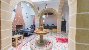 A room with a central fountain, a brick fireplace, and a patterned floor. - Riad Aylal (Essaouira)