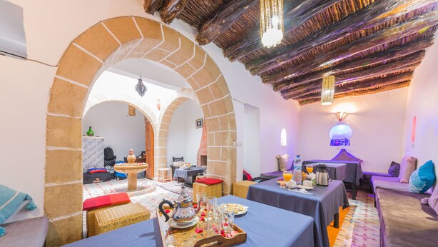A cozy dining area with tables set for breakfast, featuring a tray with a teapot and glasses. - Riad Aylal (Essaouira)
