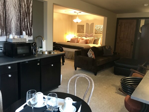 A compact living space with a kitchenette, a dining area, and a cozy seating area with a sofa and ottoman.