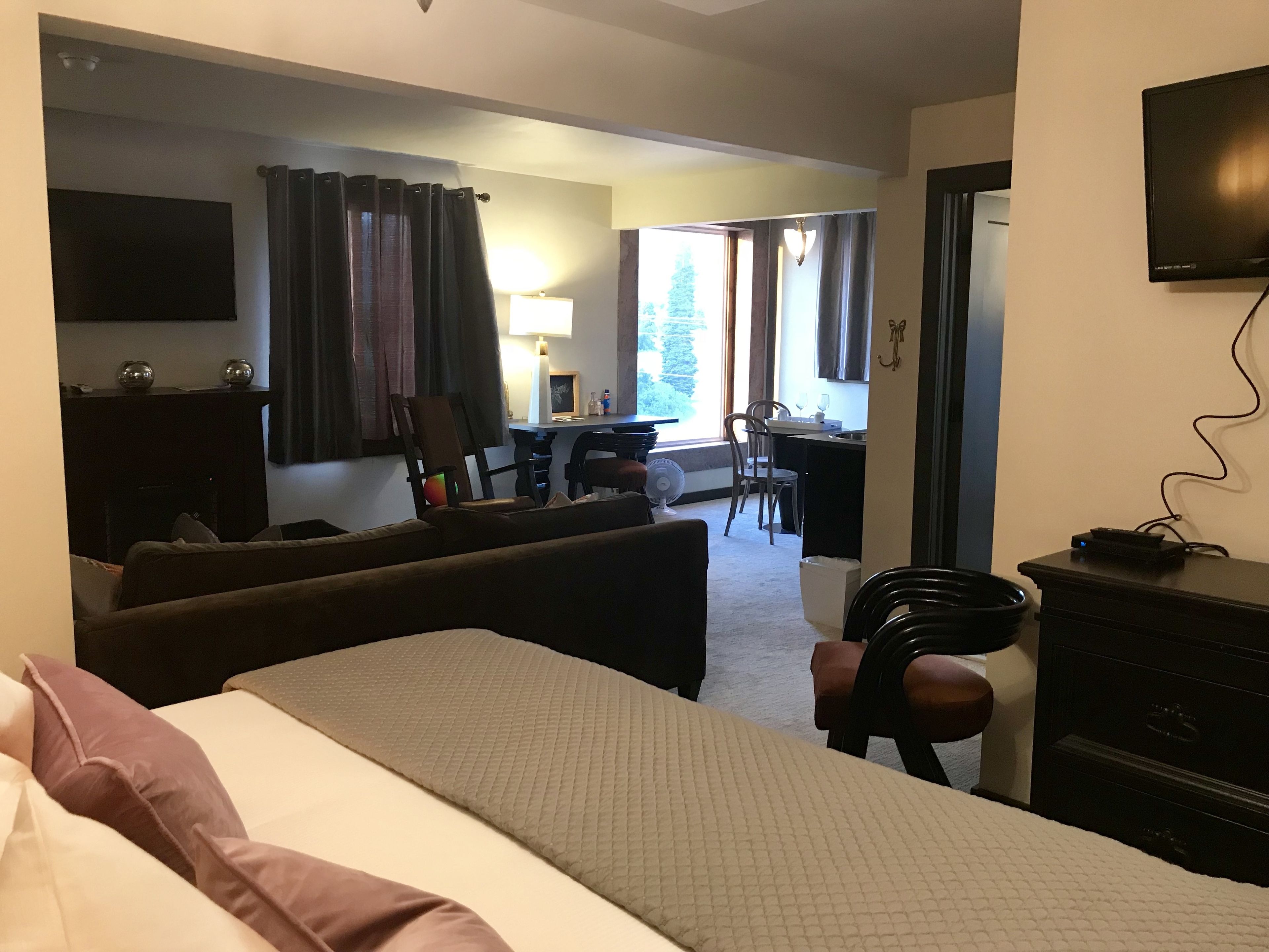 Quarto de hotel com cama, escrivaninha, cadeira, televisão e luminária.