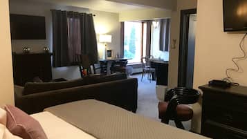 Quarto de hotel com cama, escrivaninha, cadeira, televisão e luminária.