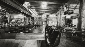 A bar with wooden floors and high ceilings, featuring a long counter and several stools. - Colter's Lodge (Afton)