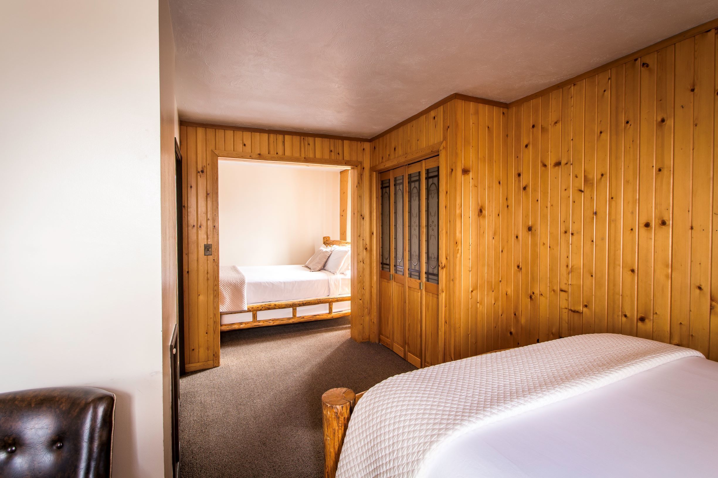 Een kamer met houten lambrisering, een bed, een stoel en een klein tafeltje.