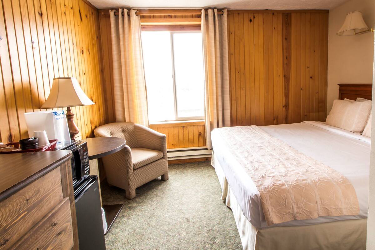 A hotel room with a bed, a chair, a desk, and a lamp.