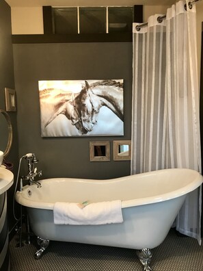 A bathroom with a freestanding bathtub, a shower curtain, a framed picture on the wall, and a mirror.