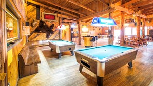 A pool hall with wooden floors, pool tables, and rustic decor including a mounted animal head. - Colter's Lodge (Afton)