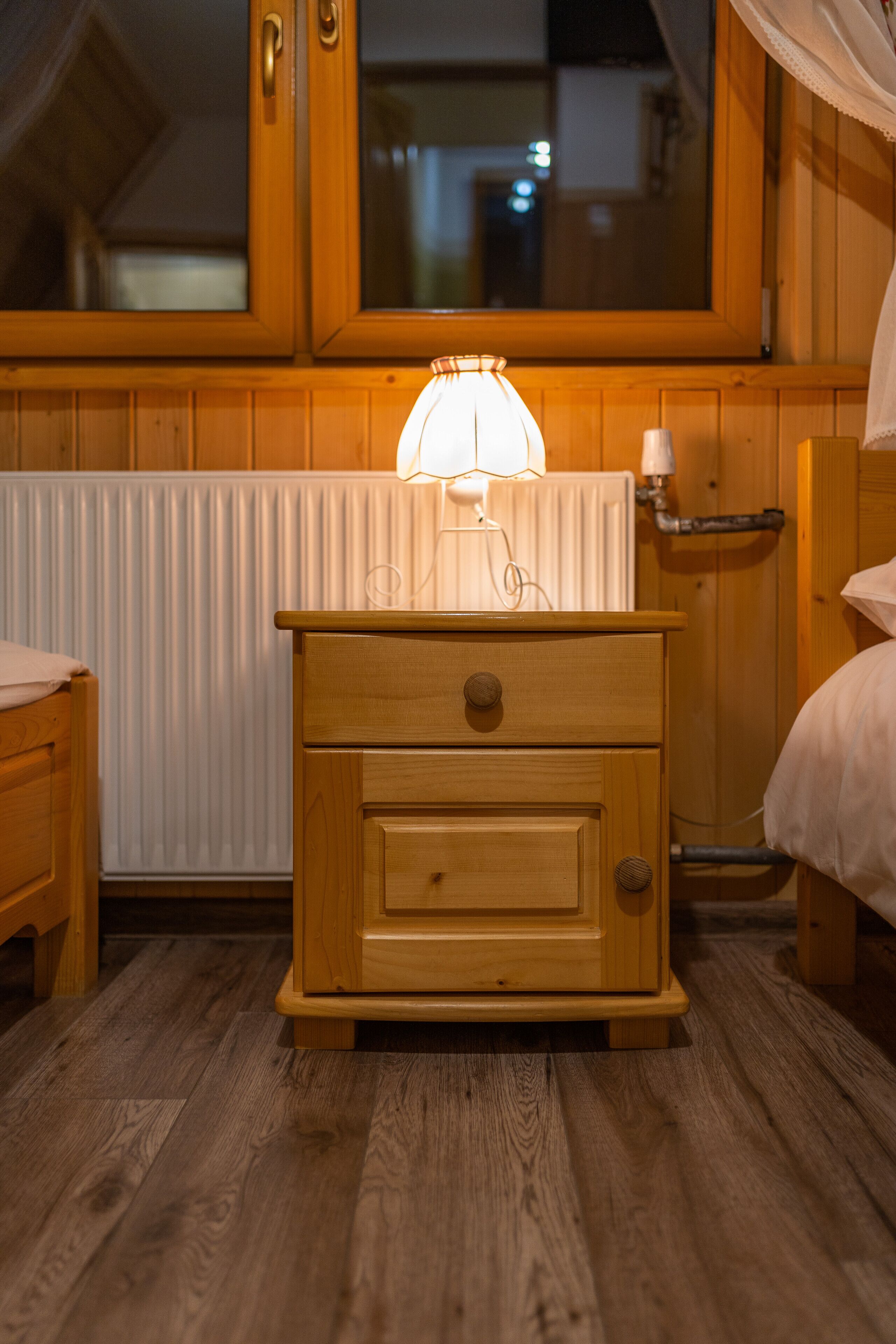 A wooden nightstand with a lamp, a drawer, and a bedside table with a white pillow.