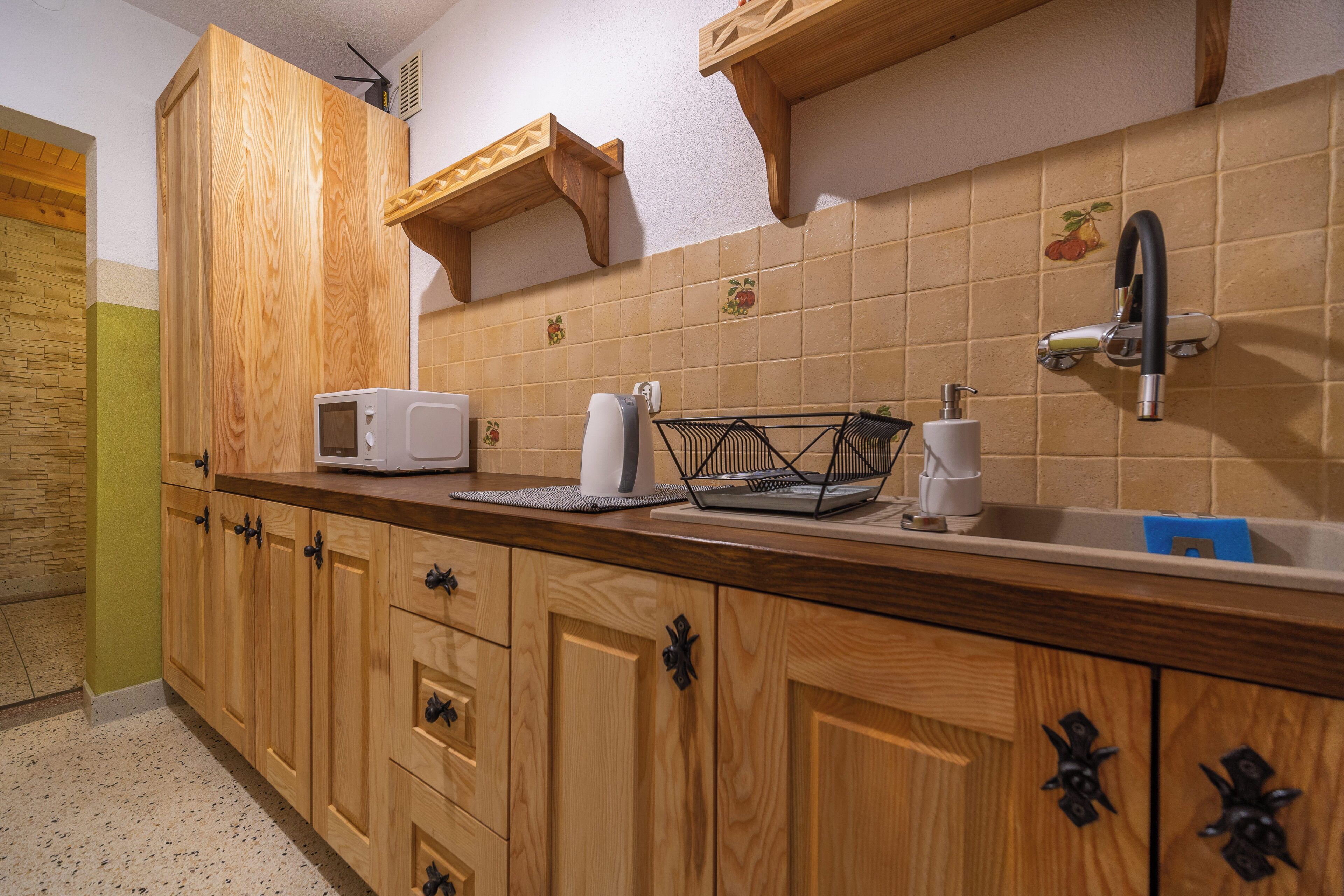 A kitchen with wooden cabinets, a microwave, a sink, and a fruit-themed backsplash.