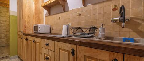A kitchen with wooden cabinets, a microwave, a sink, and a fruit-themed backsplash.