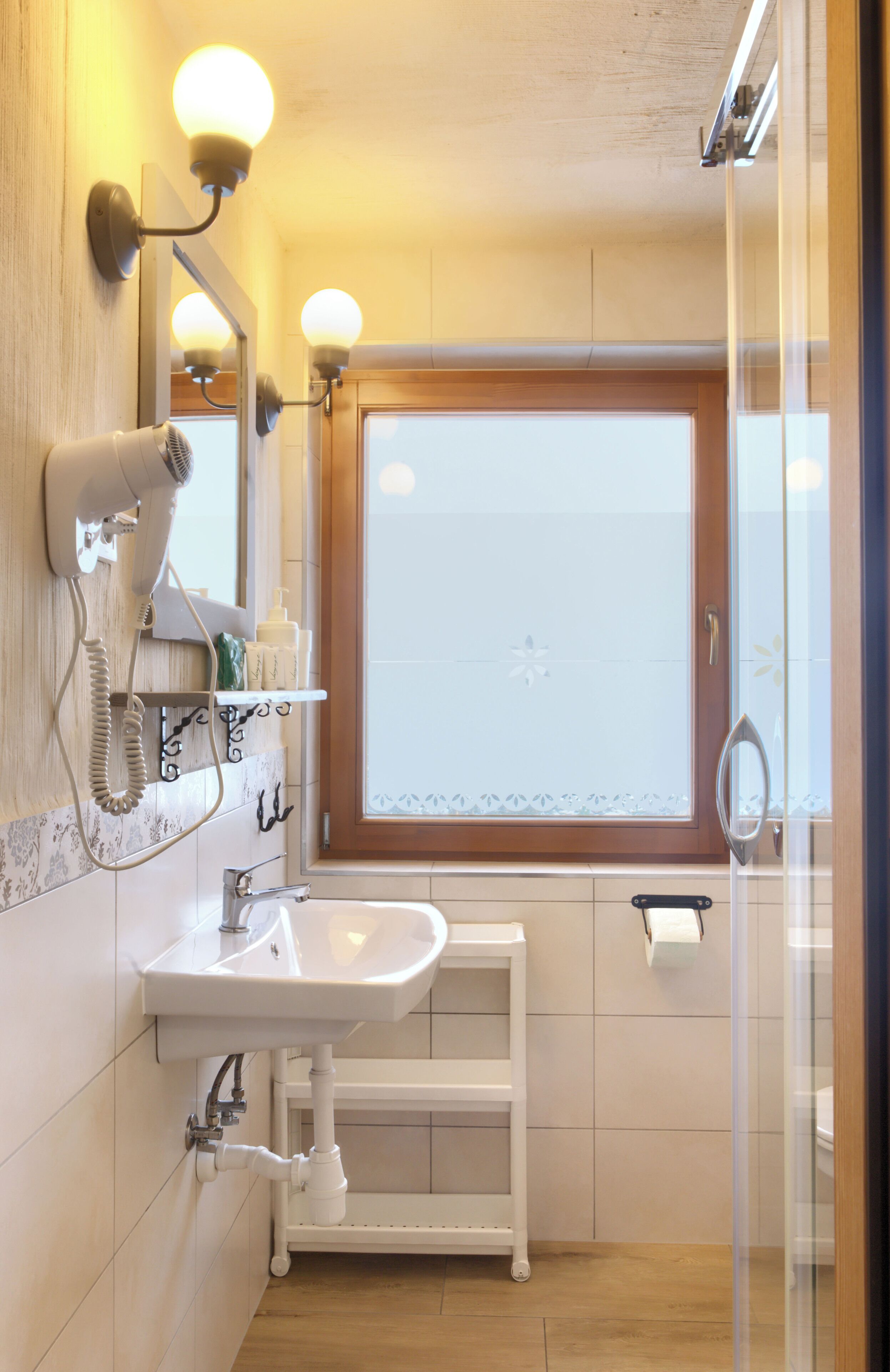 A bathroom with a white sink, a hairdryer, a mirror, and a window with frosted glass.