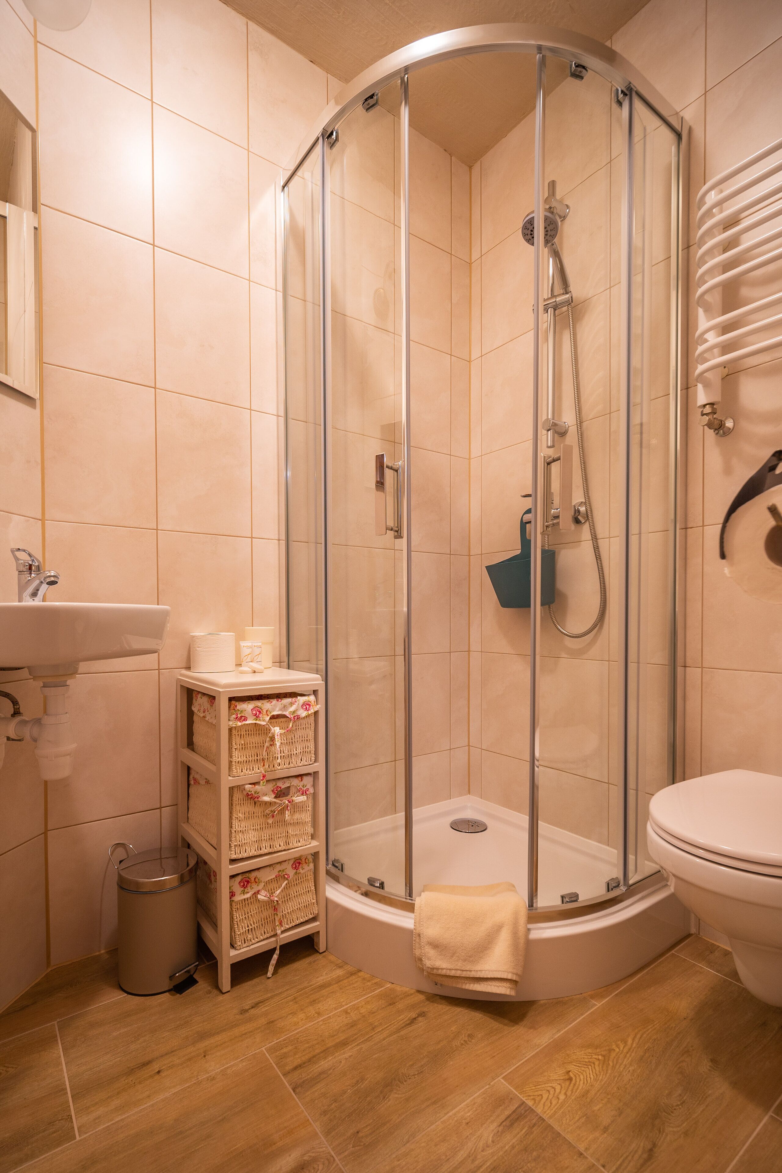 A bathroom with a glass-enclosed shower, a toilet, a sink, and wicker baskets on a shelf.