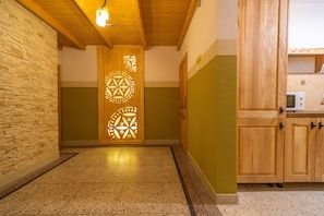 Un pasillo con pared de piedra, puerta de madera con diseño geométrico y una zona de cocina con armarios de madera y un microondas.