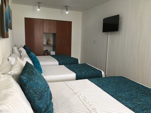 A bedroom with two beds, a wardrobe, a flat-screen TV, and a shelf with decorative items. - Regines Hotel (Manizales)