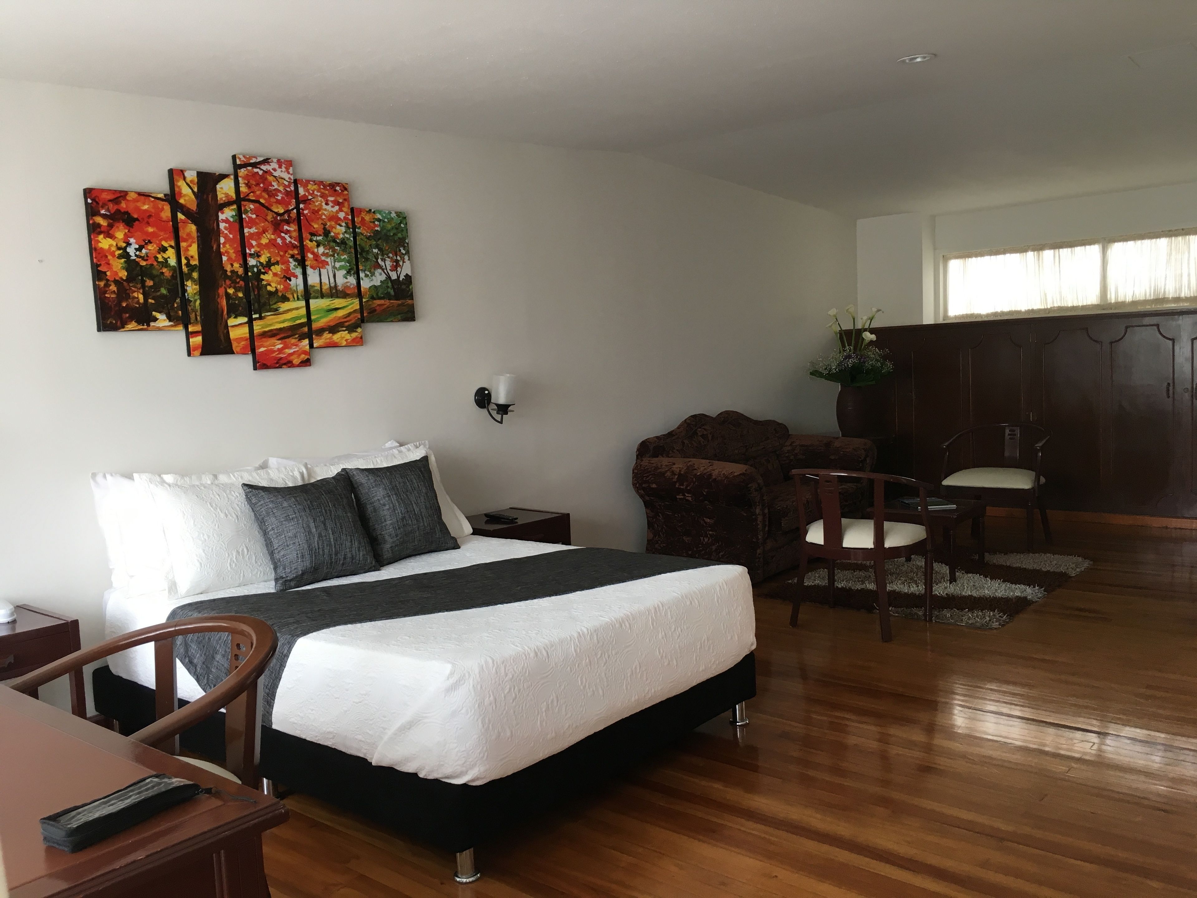 A hotel room with a bed, a desk, a chair, a sofa, a cabinet, and a window.