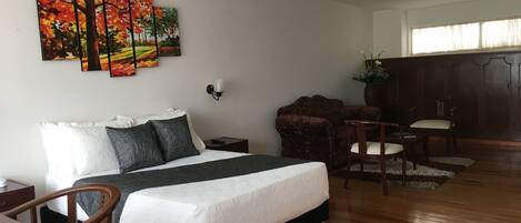 A hotel room with a bed, a desk, a chair, a sofa, a cabinet, and a window.