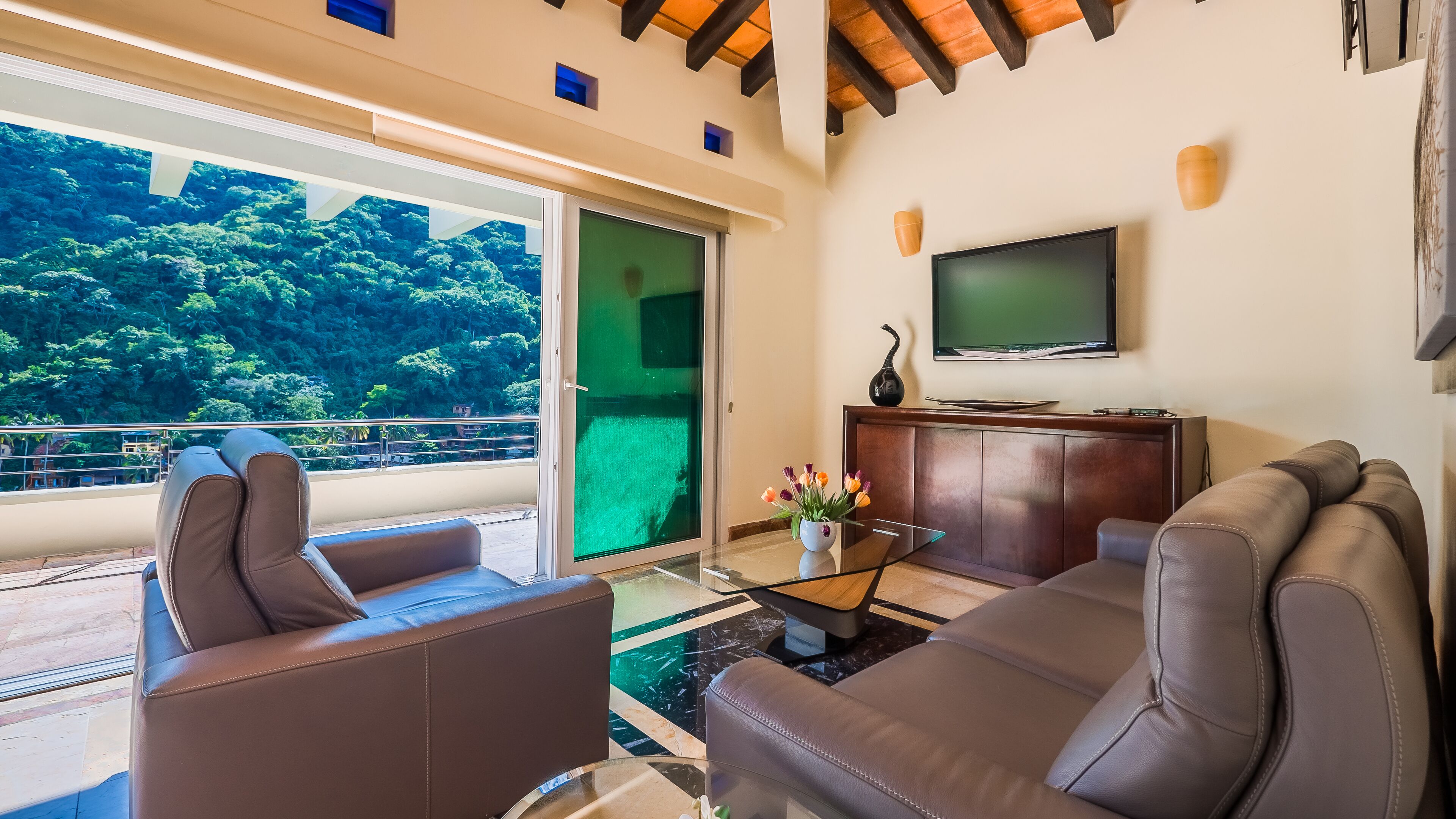 A modern living room with leather sofas, a glass coffee table, and a flat-screen TV.