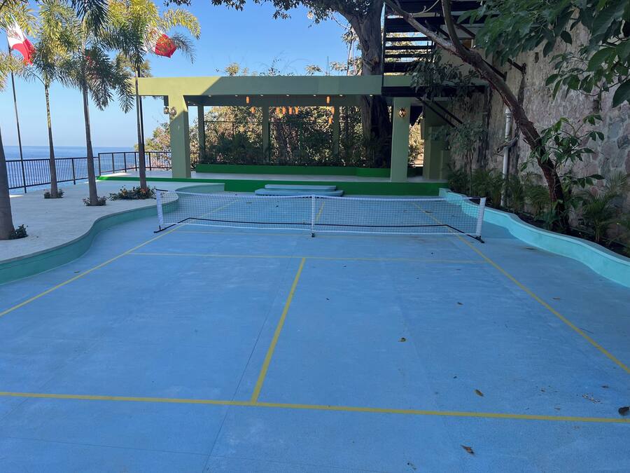 Una cancha de tenis al aire libre con una red, rodeada de vegetación y un muro de piedra.