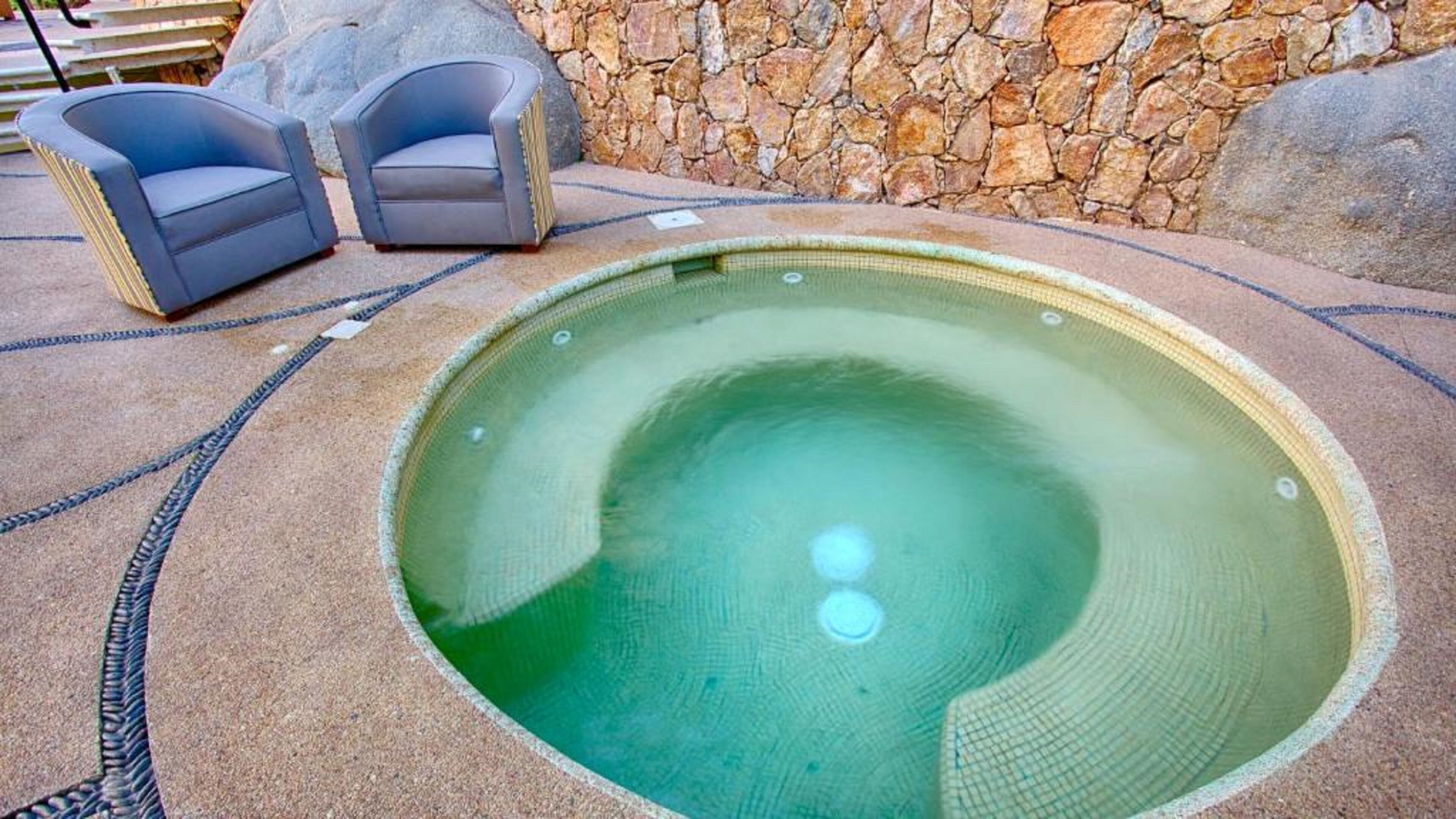 Ein Whirlpool mit Steinwand und zwei Stühlen.