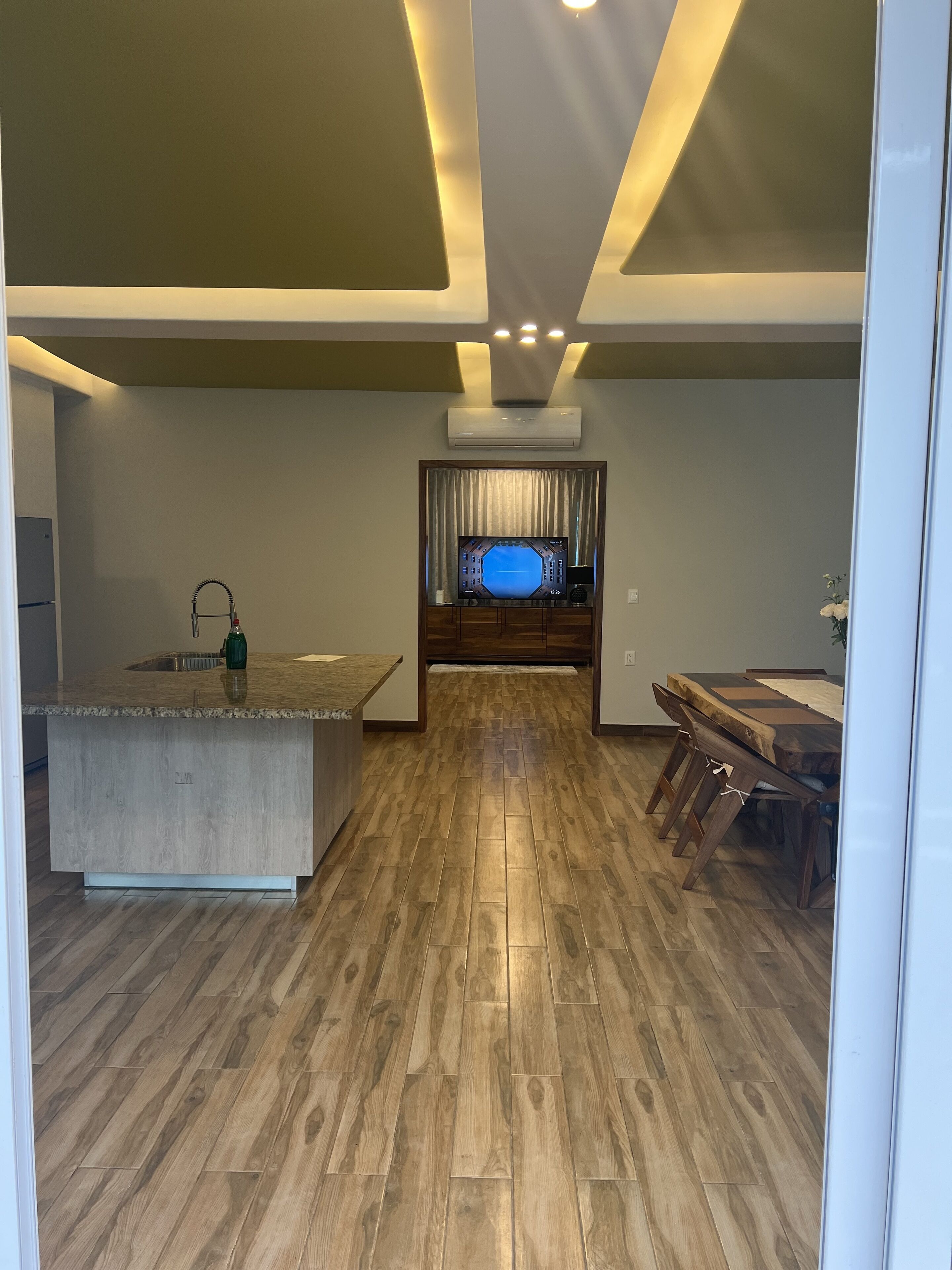 Una cucina moderna con isola centrale, pavimento in legno e illuminazione a soffitto incassata.