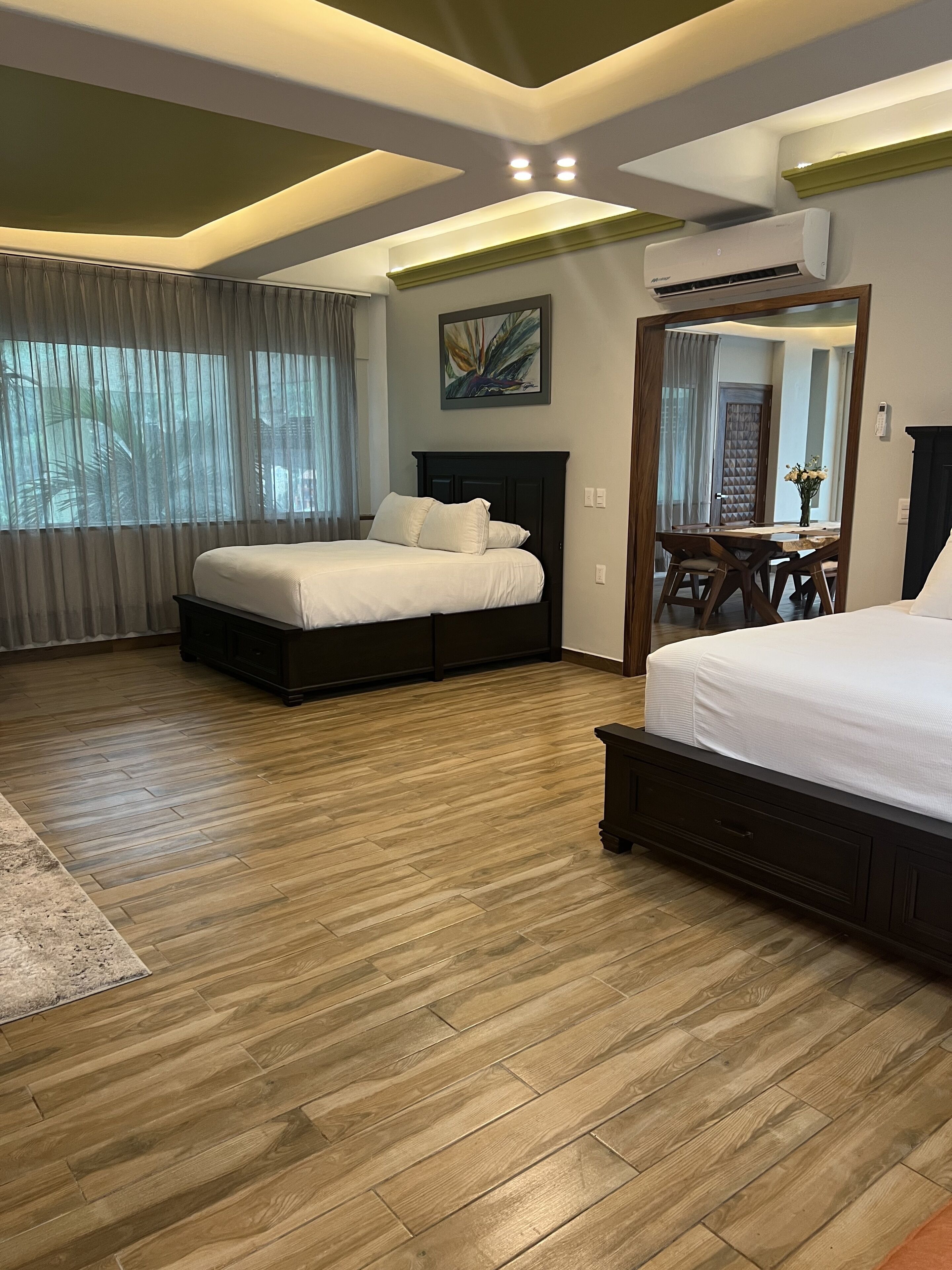 Un dormitorio moderno con suelo de madera, una cama grande con cabecera oscura, una mesita de noche y un espejo.