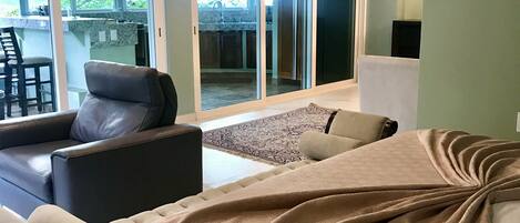 Ein modernes Wohnzimmer mit einer Couch, Sesseln und einem großen Fenster mit Blick ins Freie.