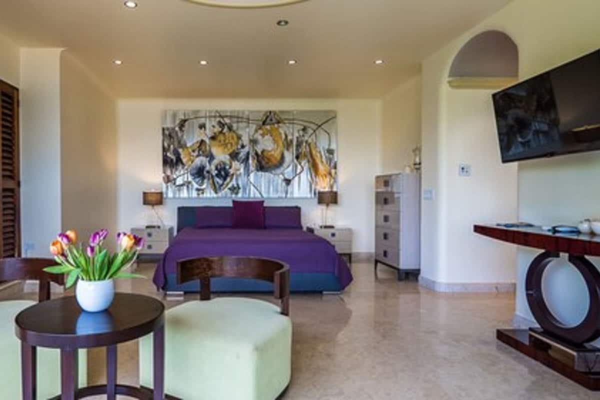 Un dormitorio amplio con una cama grande, una obra de arte moderno en la pared, un televisor y una zona de comedor con mesa y sillas.