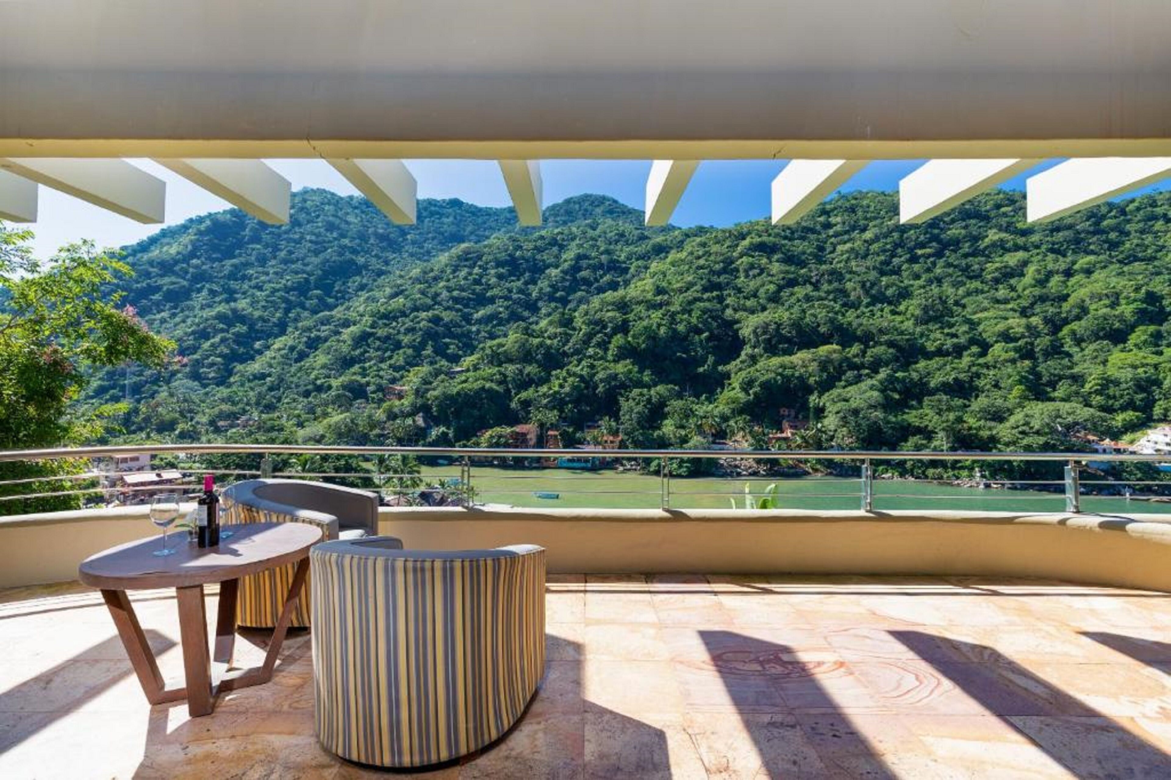 Una terraza con una mesa y asientos, con vista a un exuberante valle verde y montañas.