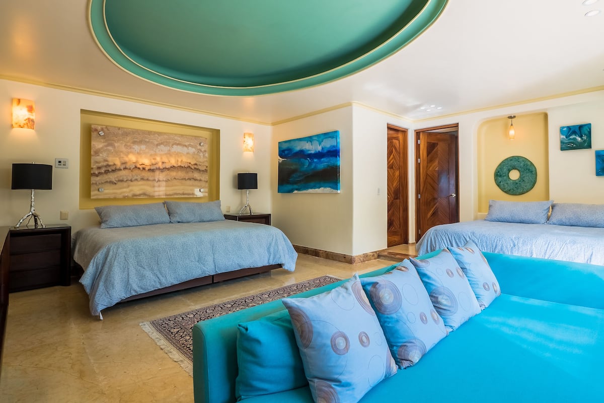 Habitación de hotel con dos camas, un cuadro abstracto de gran tamaño y una puerta de madera.