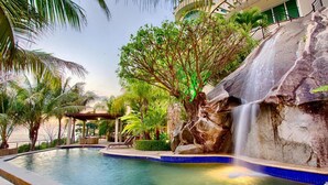 A pool area with a waterfall, palm trees, and a covered seating area. - Villa Armonia Boutique (Puerto Vallarta)