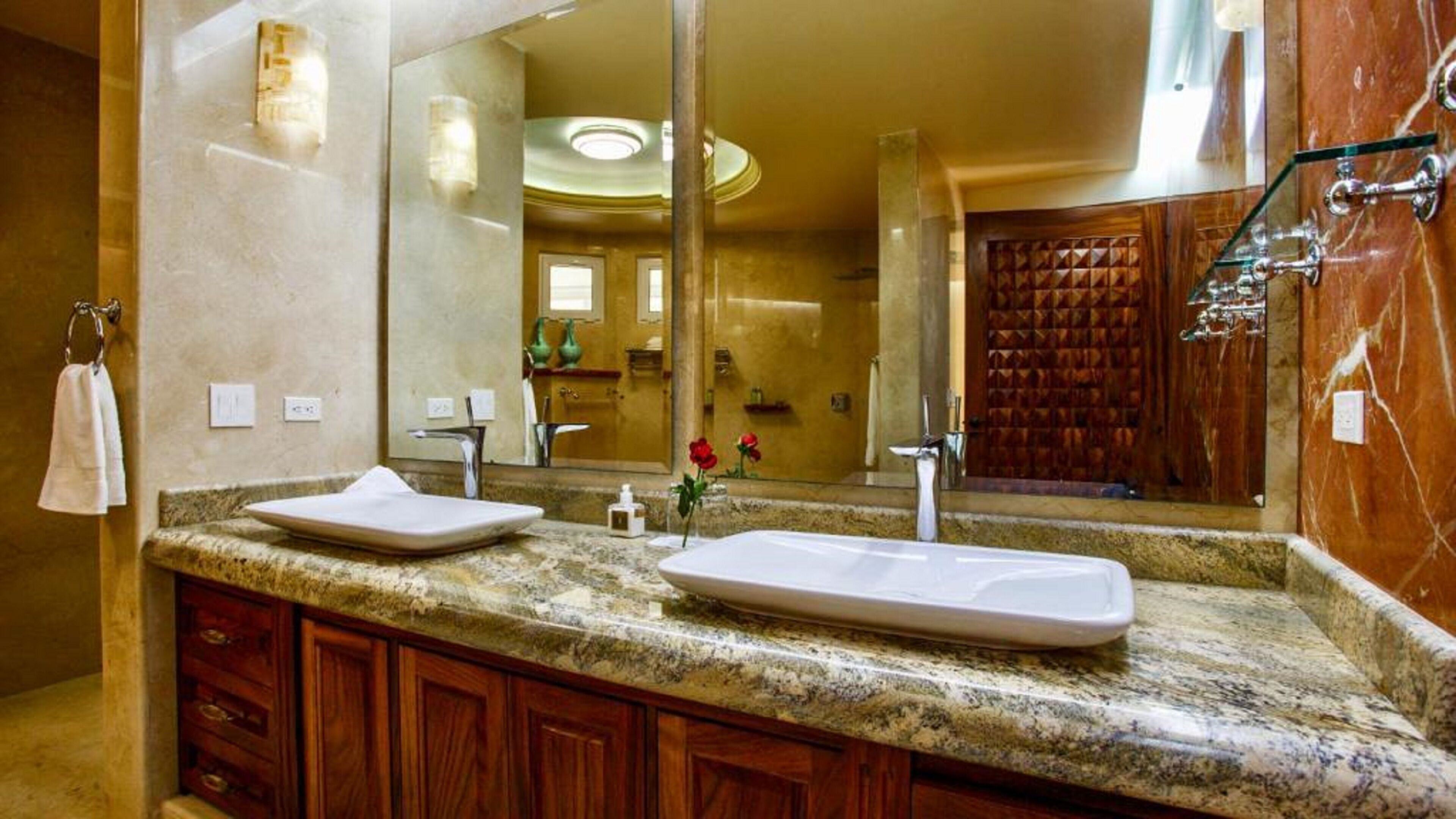 A bathroom with a marble countertop, two sinks, a large mirror, and a wooden door.
