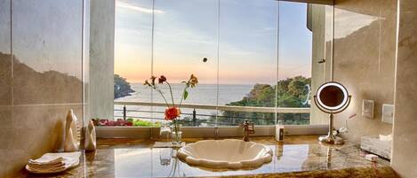 A bathroom with a large window, a marble sink, a mirror, and a view of the sea.