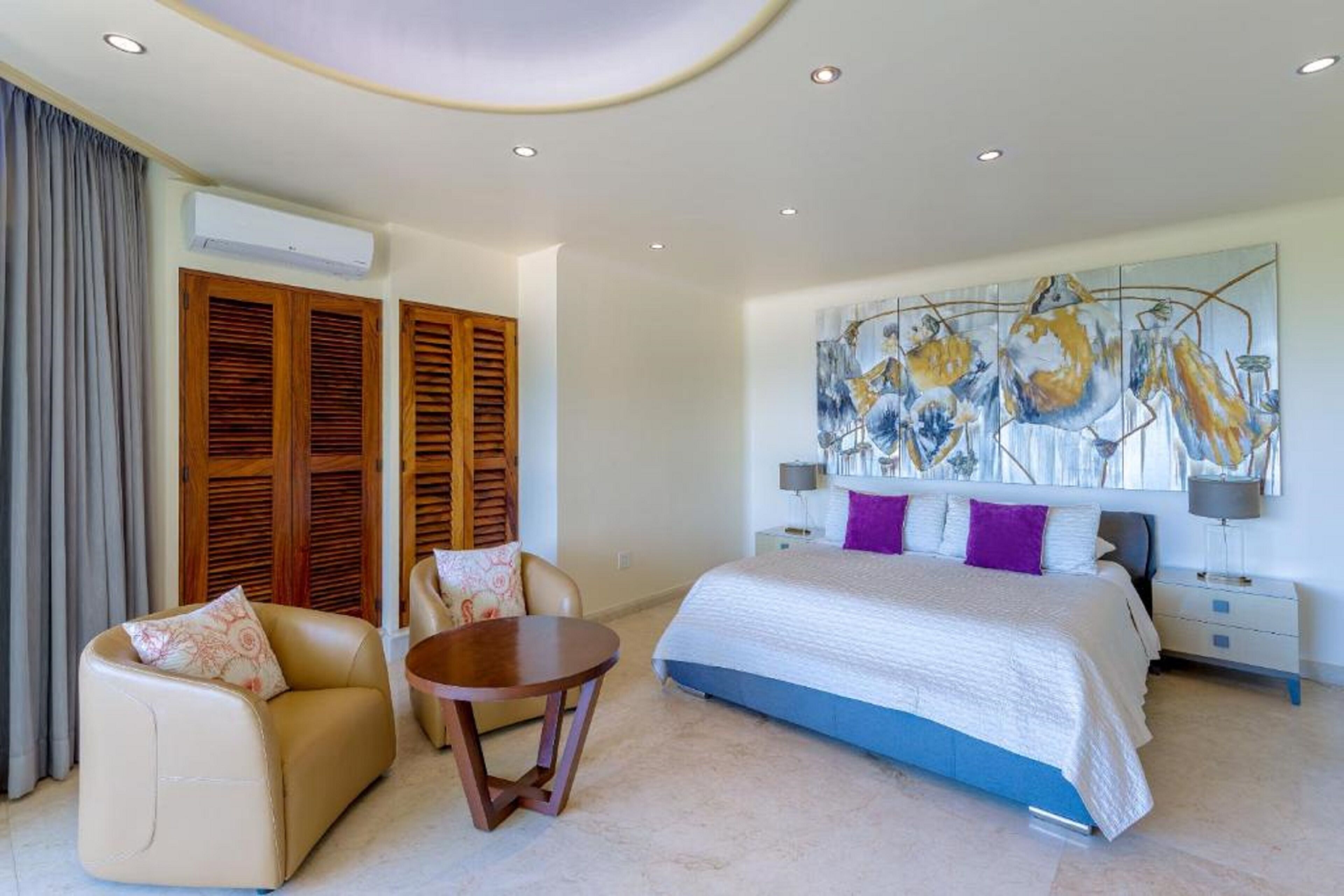 Una habitación de hotel moderna con una cama grande, un sofá, una mesita y una obra de arte en el techo.
