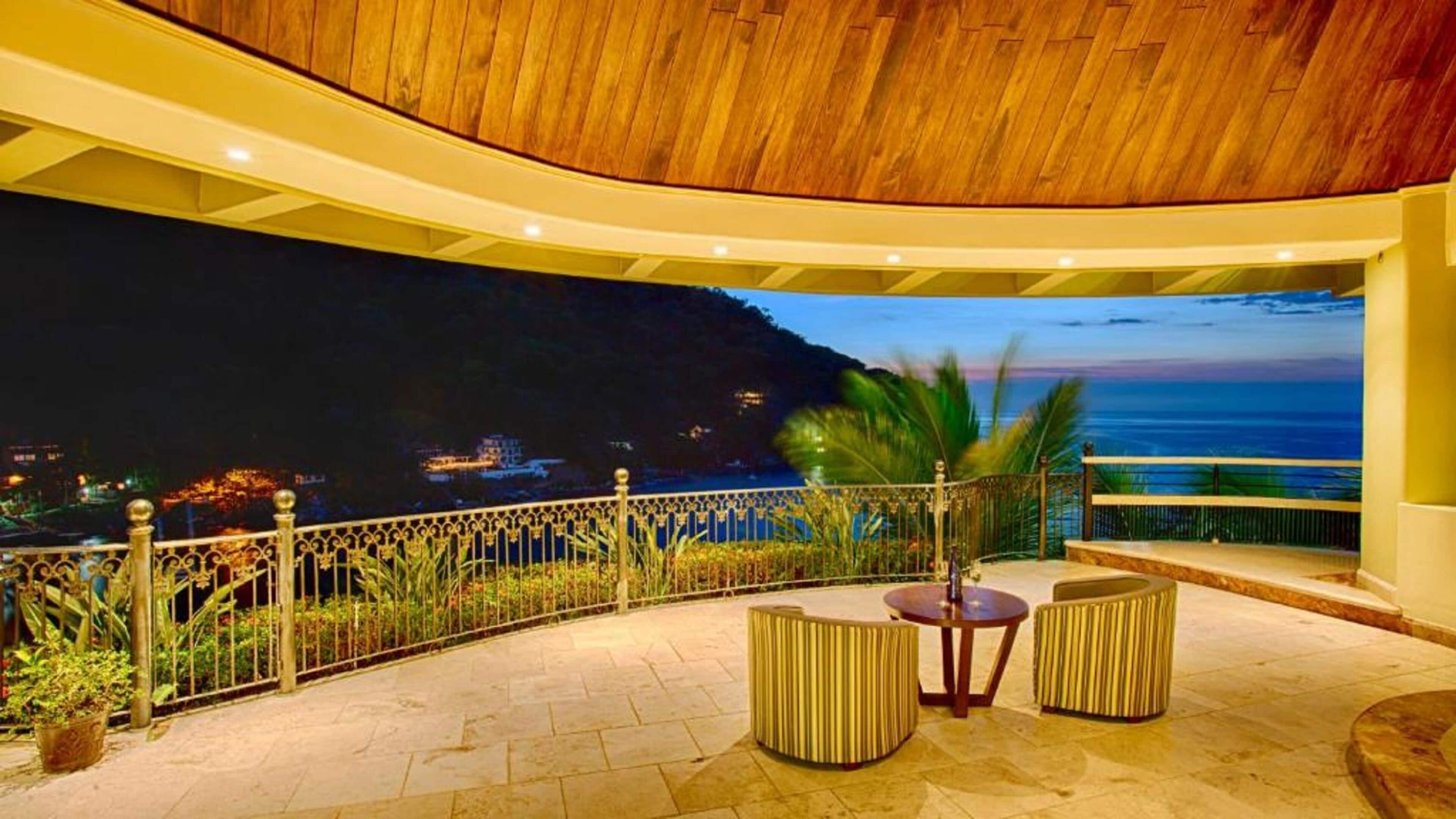 A terrace with a view of the sea, featuring a wooden ceiling, a railing, and seating.