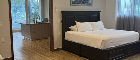 A modern bedroom with a large bed, a built-in desk, and a view of the outdoors.