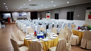 A banquet hall with rows of tables set for a meal, chairs covered with white fabric, and a stage with a podium. - Marang Village Resort & Spa (Marang)