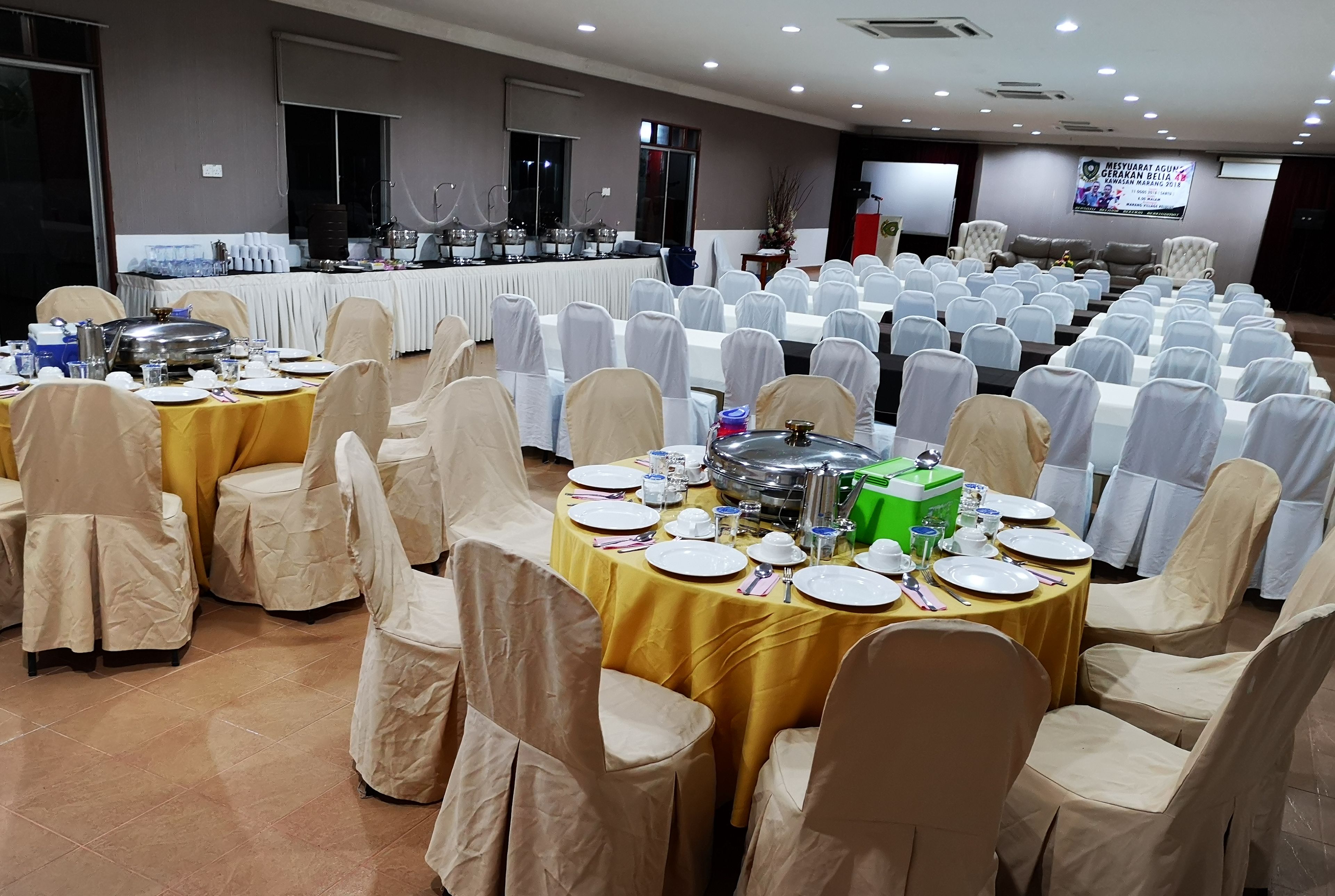 A banquet hall with round tables covered in yellow tablecloths, white chairs, and a buffet setup.