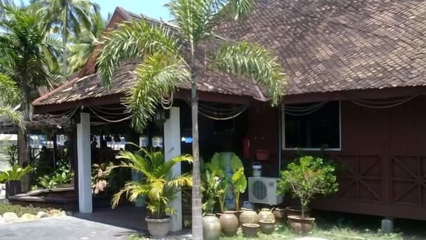 A building with a tiled roof, surrounded by potted plants and palm trees. - Marang Village Resort & Spa (Marang)
