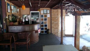A restaurant interior with a counter, wooden chairs, a brick wall, and a door leading outside. - Marang Village Resort & Spa (Marang)
