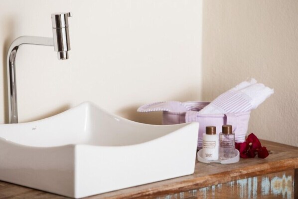 A white sink with a chrome faucet, a wooden countertop, and a small purple basket with towels and two bottles of lotion.