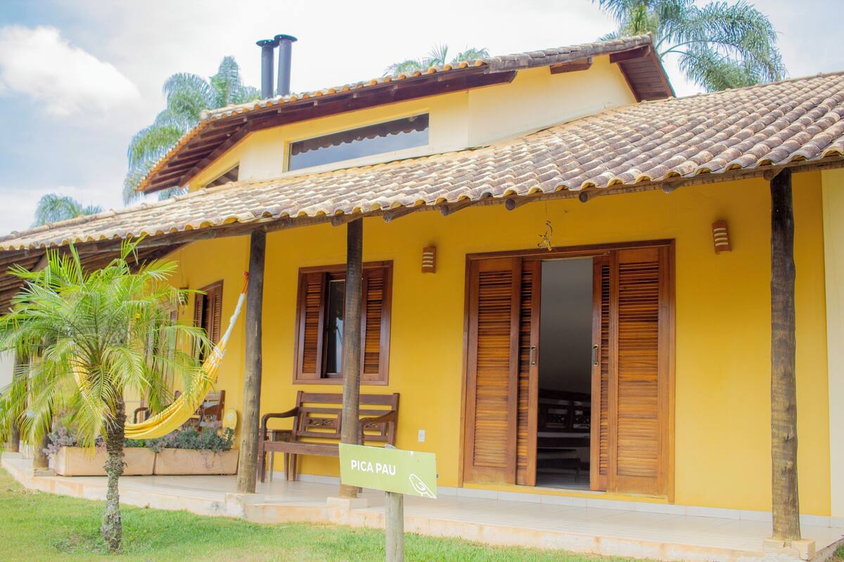 A yellow building with a tiled roof, wooden shutters, and a hammock.