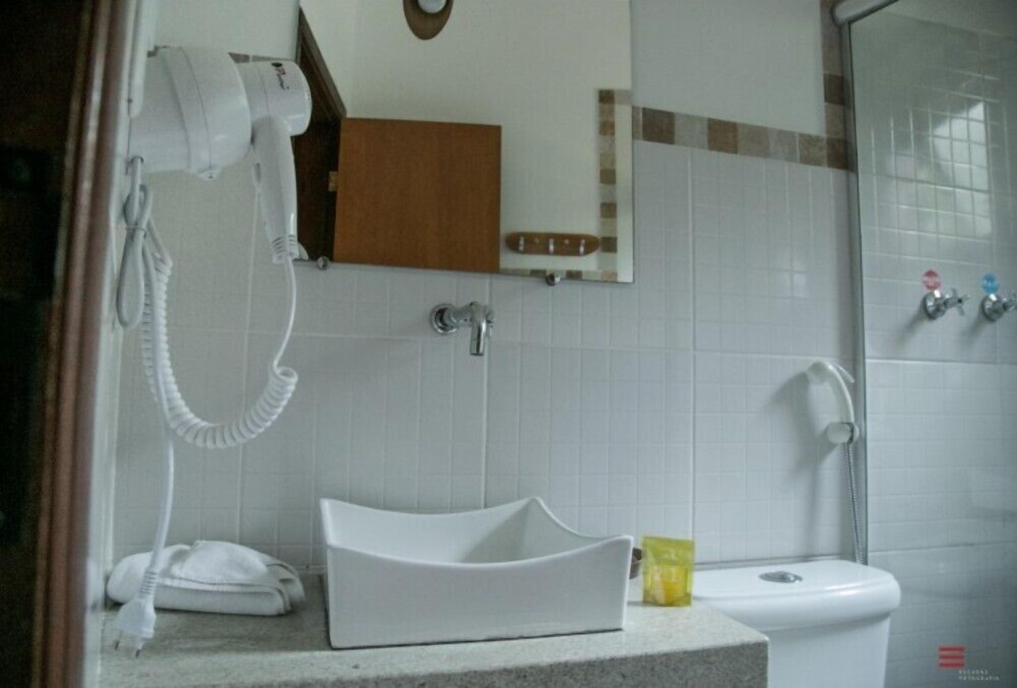 Un baño con lavamanos blanco, un espejo, una toalla, ducha y retrete.