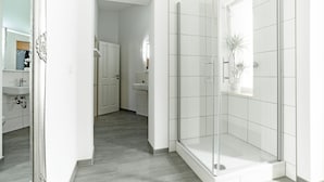Un bany modern amb una cabina de dutxa de vidre, un lavabo blanc i un mirall.