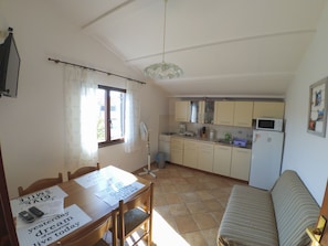 Una cocina compacta con electrodomésticos básicos, una mesa de comedor con papeles y un sofá en una habitación luminosa con ventana.